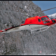 Red Helicopter Landing in the Snow at the Base of a Mountain